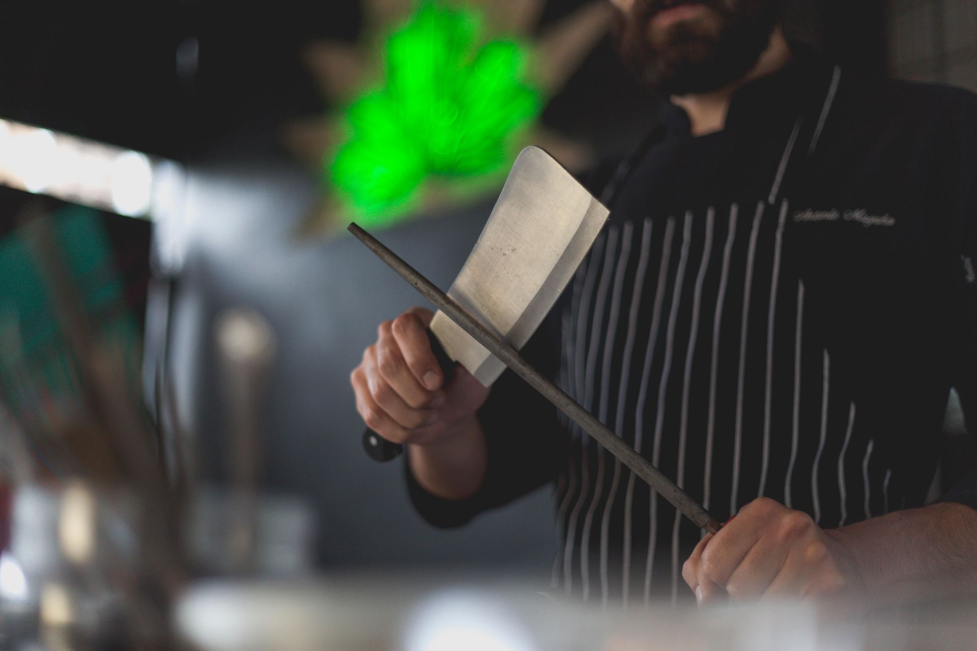 Close-up of a chef sharpening a kitchen knife with a honing steel in a professional kitchen setting.