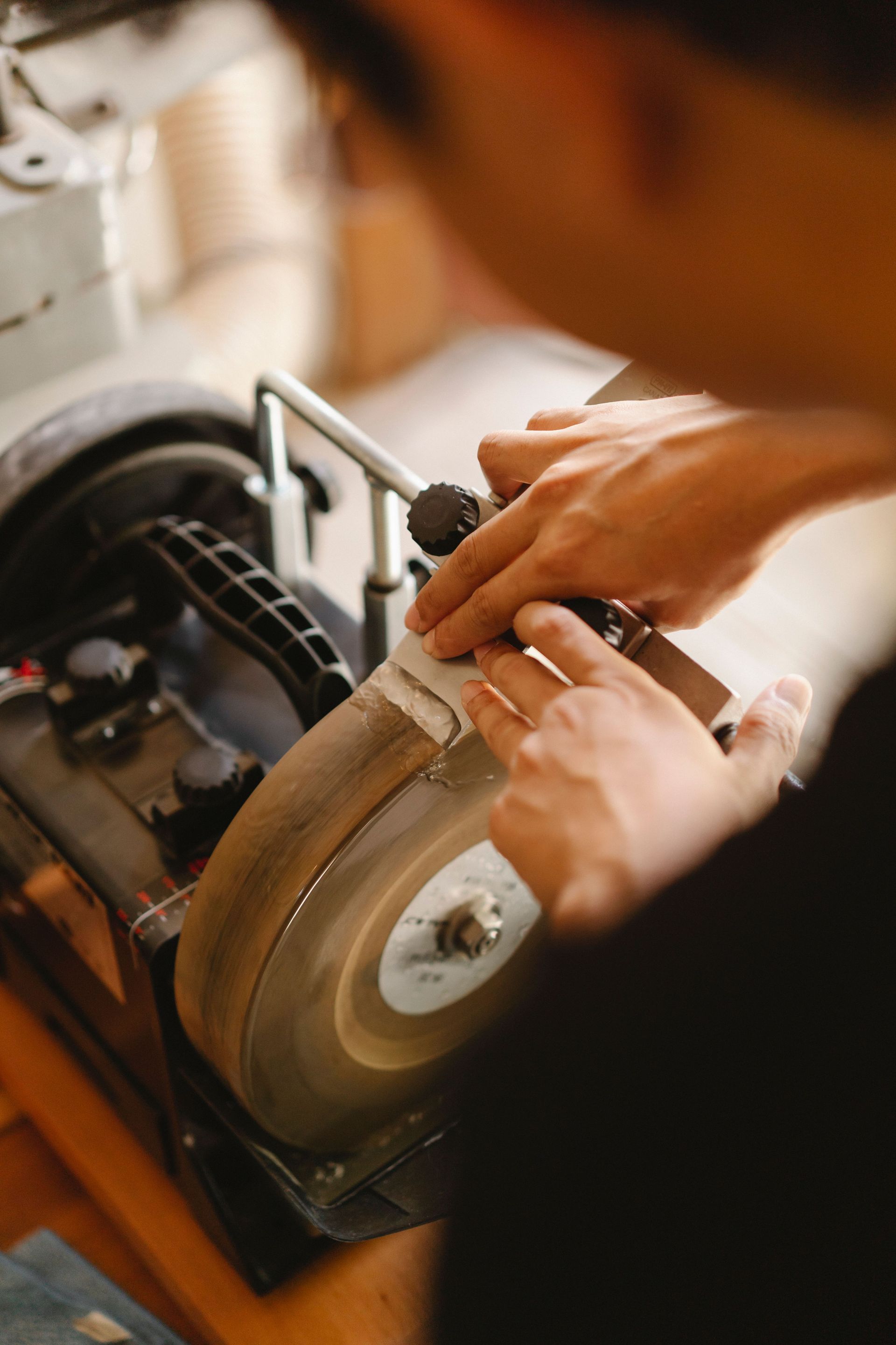 From above back view of blurred unrecognizable male master standing at sharpening machine and grinding knife while working in studio