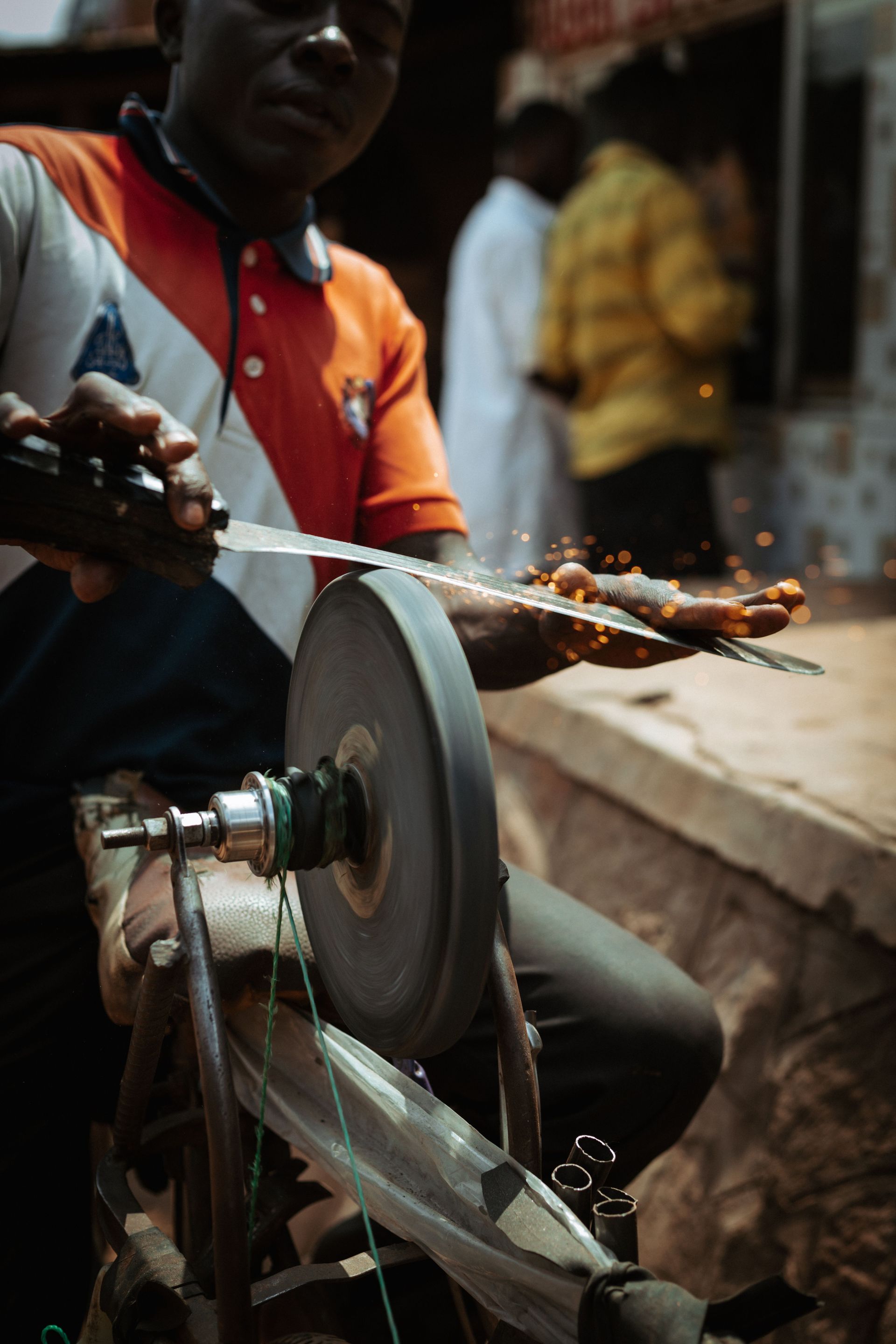 Artisan skillfully sharpens a knife with a grinder wheel, emitting sparks in an urban setting.