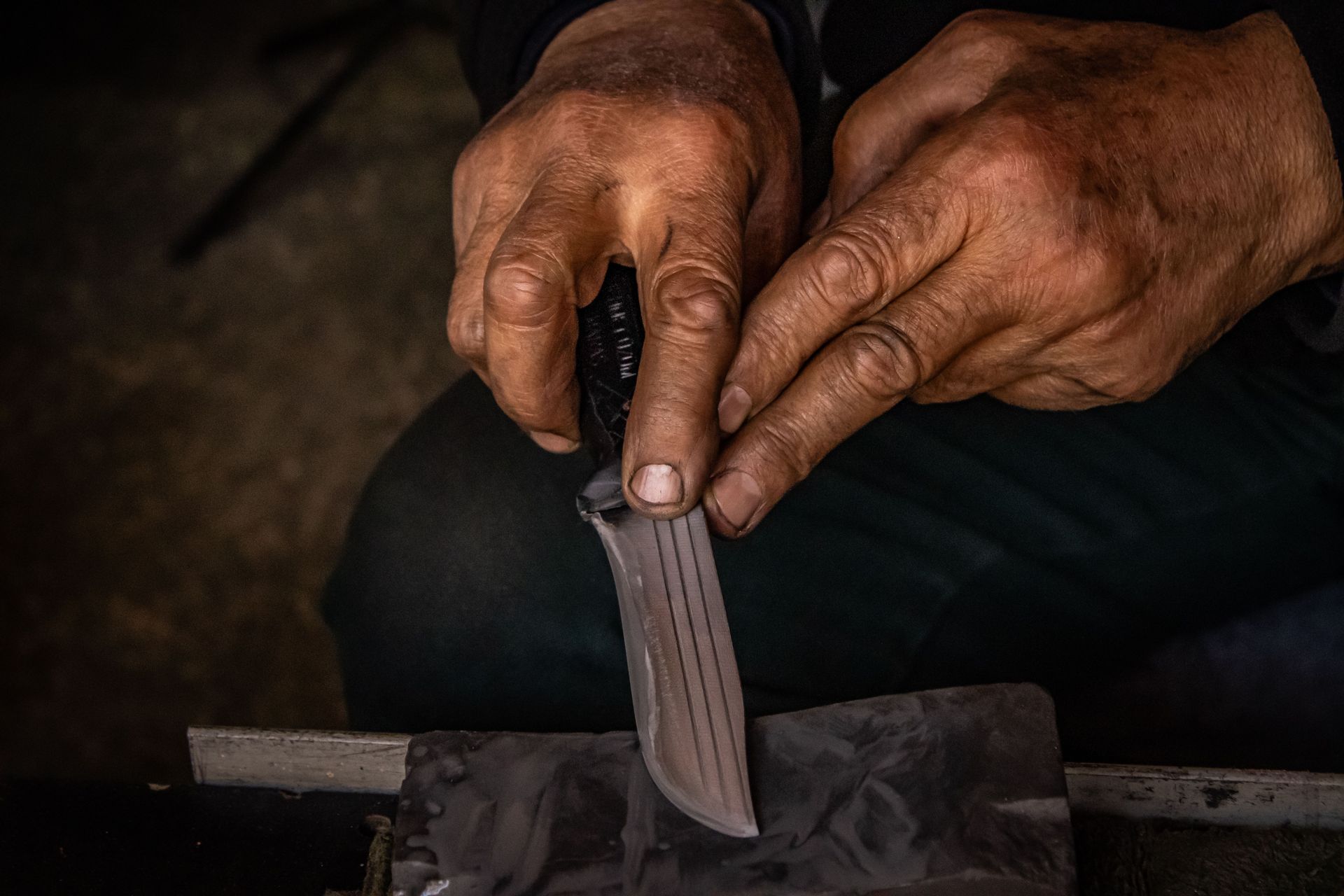 Detailed image of hands sharpening a knife using a whetstone, showing craftsmanship and precision.