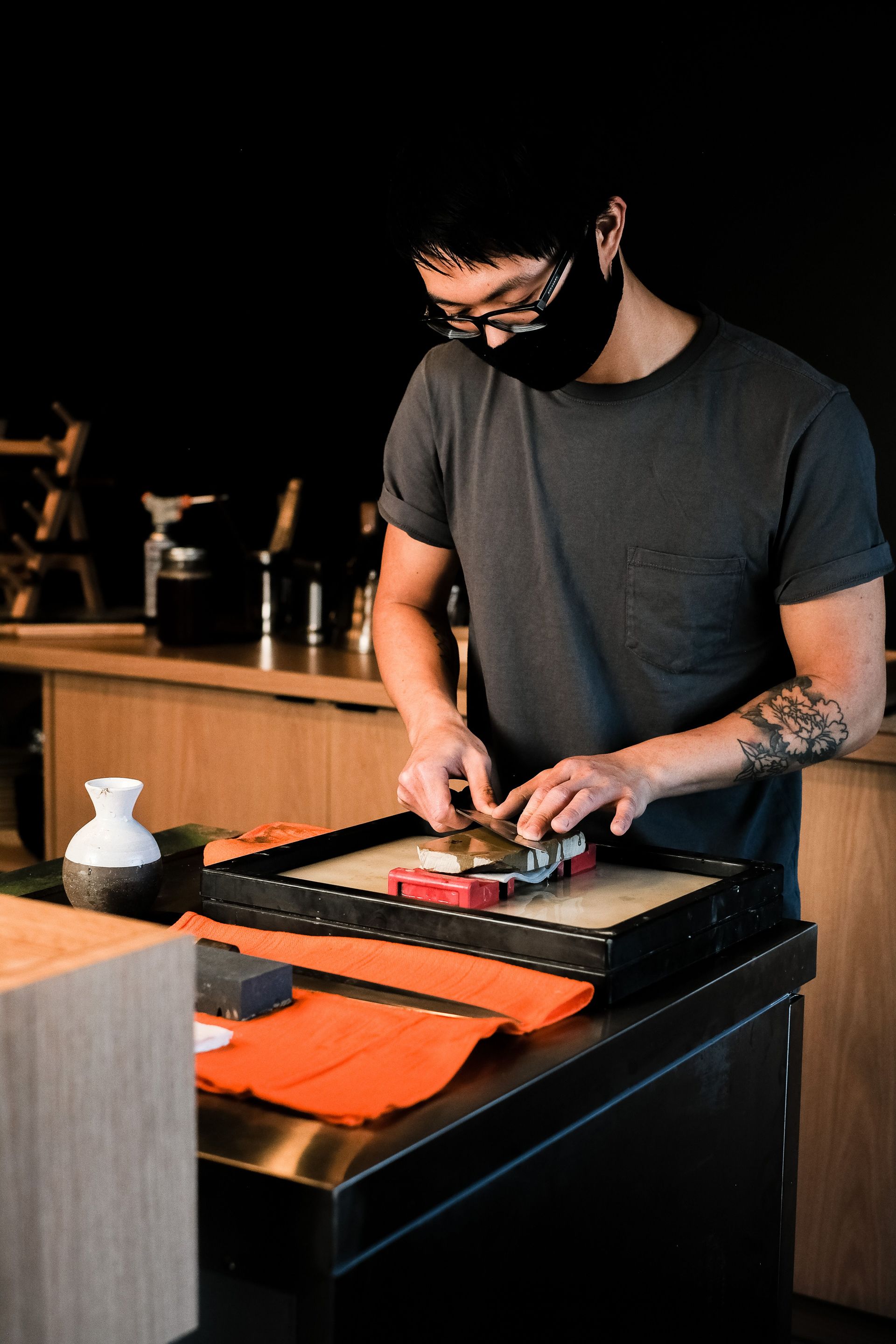Asian chef sharpening a knife indoors using a whetstone in a Japanese restaurant setting.